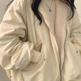 
A fashion model wearing an oversized women's black bomber puffer jacket, styled with trendy winter fashion elements. The jacket features a prominent collar and structured shoulders, paired with a dress shirt underneath. The model poses confidently, accessorized with sunglasses, showcasing the 2XL size variant in a white color.