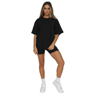 Oversized women's black cotton t-shirt in casual loose fit, knee-length, 2XL size, modeled by a person standing with one arm slightly bent and the other relaxed, showcasing the short sleeves and comfortable fit.