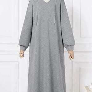 
A woman wearing an oversized long gray hoodie dress made from a comfortable cotton blend, featuring long sleeves and a casual collar.
