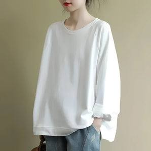 
A woman wearing an oversized white sweater made of a casual cotton blend, paired with a dress shirt underneath. The sweater features long sleeves and the image focuses on the torso area up to the waist.