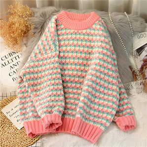Pastel knit sweater featuring a multicolor diamond pattern with pink trim, displayed on a clothes hanger. The sweater has a cozy vintage style and is shown in a pink color variant, size 3XL, highlighting its tartan-like design with long sleeves.