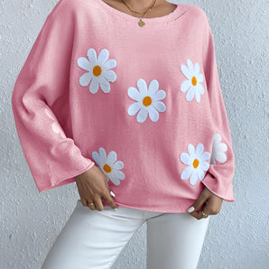 Oversized pastel pink sweater with a daisy print design, featuring a woman's hand and arm modeling the soft knit fabric.