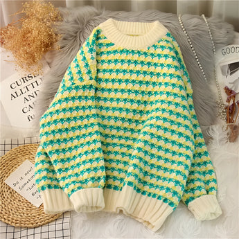 A cozy soft knit pullover sweater featuring a pastel pink and green houndstooth pattern, displayed in a 3XL size. The garment is hanging on a clothes hanger, showcasing its long sleeves and comfortable design.
