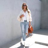 Woman wearing a peach lace blouse and acid wash jeans, paired with white sneakers, posing in a stylish summer outfit. She is accessorized with sunglasses and carrying a bag, showcasing a chic, casual look.