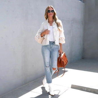 Woman wearing a peach lace blouse and acid wash jeans, paired with white sneakers, posing in a stylish summer outfit. She is accessorized with sunglasses and carrying a bag, showcasing a chic, casual look.