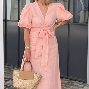 Peach linen V-neck wrap dress worn by a mature woman smiling and wearing white sunglasses, showcasing elegant summer fashion.