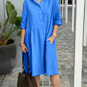 Peach mid-length spring dress for women, casual and lightweight with an elegant design, displayed in a blue variant, size 3XL, worn by a smiling model standing next to a white flowerpot containing a green houseplant, suggesting a bright, spring atmosphere.