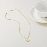 A close-up of a Pearl Centerpiece Necklace designed by YA-CHAN, featuring a gold floral pendant, displayed elegantly on a white porcelain dish.