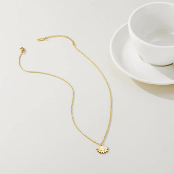 A close-up of a Pearl Centerpiece Necklace designed by YA-CHAN, featuring a gold floral pendant, displayed elegantly on a white porcelain dish.