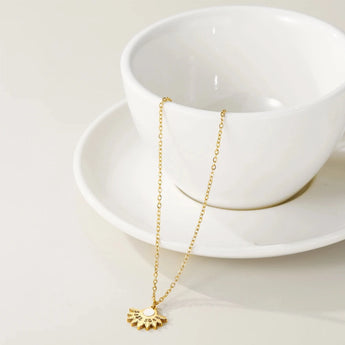 Pearl centerpiece necklace with gold floral pendant displayed on a soft background.