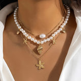 Elegant pearl necklace featuring gold starfish and seashell charms, worn around the neck.