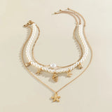 Pearl necklace with gold starfish and seashell charms, elegant beach jewelry displayed on a neutral background.