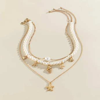 Pearl necklace with gold starfish and seashell charms, elegant beach jewelry displayed on a neutral background.