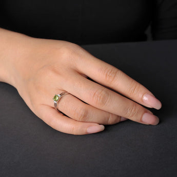 Sterling silver ring with a cushion-cut green peridot gemstone and small diamonds on a person's finger.