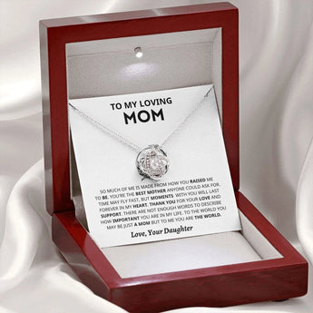 Personalized heart-shaped silver necklace displayed in a box with a picture frame and perfume in the background, perfect Mother’s Day gift from daughter.