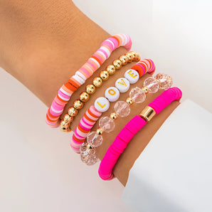 A stack of five pink beaded bracelets with love letter charms on a wrist, showcasing stackable summer jewelry.