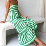 Pink and blue striped spaghetti strap maxi dress designed for summer beachwear, showcasing a flowing silhouette with a fitted waist and ankle-length hemline. Model accessorizes with casual sandals.