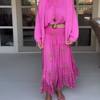 Woman wearing a pink boho skirt paired with an oversized sweater, showcasing women's spring fashion. The outfit is complemented by her joyful smile, highlighting the magenta and purple hues in the ensemble.
