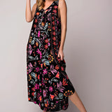 A wide-leg jumpsuit featuring a pink floral bohemian design with pockets, shown on a model. The jumpsuit has short sleeves and a flattering waistline, ideal for casual or day wear. The model is accessorized with a hat and footwear, complementing the bohemian style.