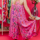 Pink floral bohemian wide-leg jumpsuit with pockets, featuring a vibrant pink floral pattern, loose wide-leg fit, and comfortable waist, worn by a smiling woman with long sleeves, showcasing a relaxed and stylish bohemian vibe.