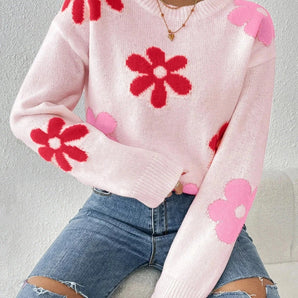 
A pink floral lightweight knit sweater featuring a red flower pattern, styled as a pullover. The sweater is paired with blue jeans, highlighting the casual yet stylish look. The sweater is in size XL, with long sleeves and a comfortable fit.