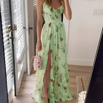 Pink floral maxi dress with a v-neck design, featuring a summer garden pattern. The dress is displayed in a green color variant and is size XL. It showcases a flowing one-piece garment style with sleeves, extending down to the knees, accentuating the waist. The dress is positioned against the backdrop of a door.