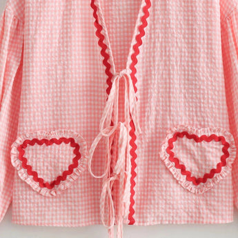 Pink gingham puff sleeve blouse with ruffle trim, featuring a vibrant spring design, displayed on a hanger against a neutral background.