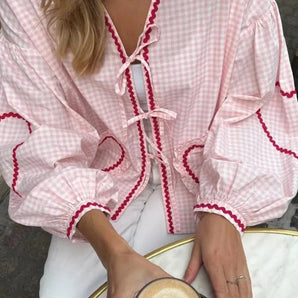 Pink gingham puff sleeve blouse with ruffle trim, showcasing close-up details of the fabric and sleeve design against a white background.