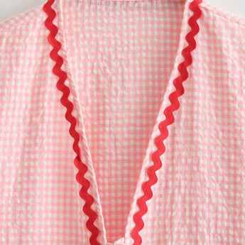 A pink gingham puff sleeve blouse with ruffle trim, featuring a spring fashion design.