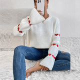 A white long-sleeve sweater with heart patterns on the sleeves, paired with jeans, showcasing a casual fall fashion look.