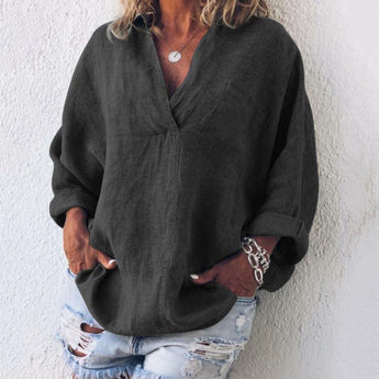 
A woman wearing a black oversized V-neck blouse made from linen, showcasing its relaxed fit with long sleeves and a comfortable, casual style.