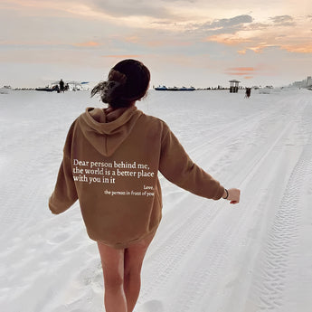 A person wearing a pink tie-dye hoodie with a motivational self-love quote, standing outdoors under a partly cloudy sky. The hoodie features long sleeves and appears to be comfortable and casual, perfect for travel or outdoor activities. The wearer looks happy, embodying a positive and inspirational vibe.