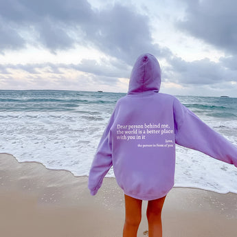 Pink tie-dye hoodie featuring an inspirational self-love quote, worn by a smiling person enjoying a beach setting with a cloudy sky in the background.