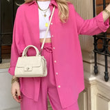 Woman wearing a pink trouser suit with high-waist pants, a blazer, and a crop top, standing in a stylish pose.
