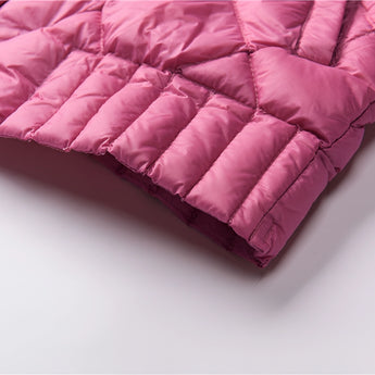 Pink women's lightweight quilted jacket with a diamond pattern, displayed on a couch with decorative pillows in the background.