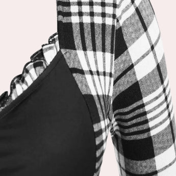 A woman wearing a black and white checkered plaid dress with long sleeves and a knee-length hemline. The dress features a collar and is styled with a fitted waist, showcasing a classic and timeless tartan pattern.
