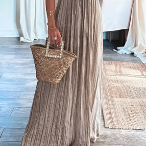 Pleated maxi dress in beige shimmer fabric, designed as an elegant evening gown suitable for a beach wedding, featuring long sleeves and a flattering waist.