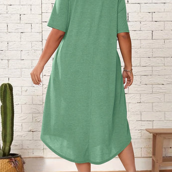 Plus size green loose fit midi dress with short sleeves, featuring an oversized casual design perfect for summer wear. The dress is displayed on a model standing and gesturing, highlighting the relaxed fit around the waist and knee length.