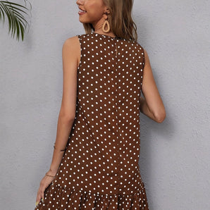 Woman wearing a sleeveless high-neck summer dress with polka dots and a ruffle hem, standing with one hand on her hip.