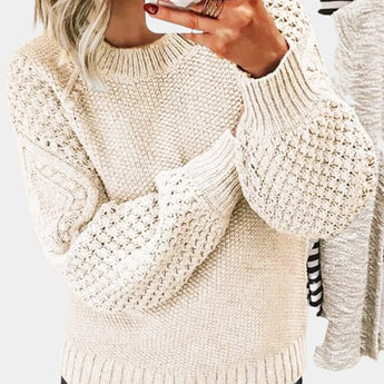 
Woman wearing a chunky cable knit sweater in a soft lavender color, featuring long sleeves and a cozy, textured design. The sweater has a high neckline and is styled to be oversized, providing a relaxed fit. The woman's arms are gently resting by her sides, showcasing the sweater's detailed knit pattern.