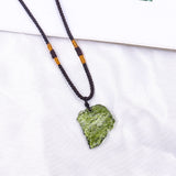 A raw moldavite healing pendant featuring a green tektite crystal on a necklace, displayed against a natural background with twigs.