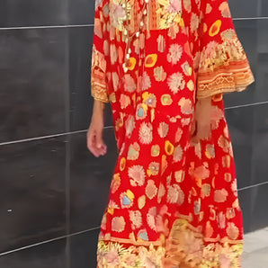 
A woman wearing a red floral bohemian kaftan dress with tassels, featuring a loose fit and flowing sleeves, suitable for summer wear. The dress showcases a vibrant pattern and an orange hue, highlighting the neckline and collar area.