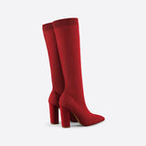 Red knee-high sock boots with high heels made from ribbed fabric, shown on a model's legs seated in a chair.