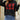 
A chic black pullover sweater featuring a bold red lip print design, worn by a model. The sweater is styled with eyewear and showcases a comfortable fit with visible shoulder and arm details.