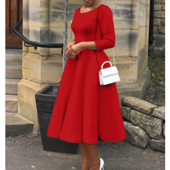 Woman wearing a red midi dress with long sleeves, a boat neck, A-line silhouette, and pockets, standing and showcasing the fit around the waist, size 2XL.