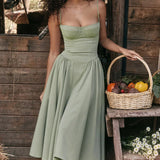 
A moss green vintage-style tea dress with spaghetti straps, designed as a midi length one-piece garment. The dress is styled for casual day wear and features a flattering waistline. The image captures the dress in a standing pose with bright lighting highlighting its elegant design.