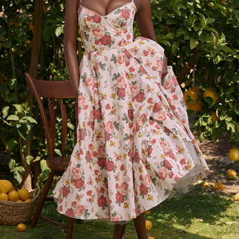 Vintage style red rose print fit and flare dress designed for garden parties, featuring a one-piece garment with a flattering waist, short sleeves, and a round neckline, set against a backdrop of lush grass.