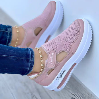 A pair of red slip-on platform sneakers with breathable cut-out design and chain detail, showcased on a model wearing the shoes. The image focuses on the footwear, highlighting its stylish features and comfortable fit.