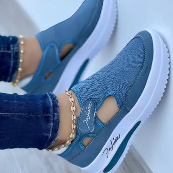 Pair of blue slip-on platform sneakers featuring breathable cut-out details and decorative chain accents, shown being worn on a person's feet.
