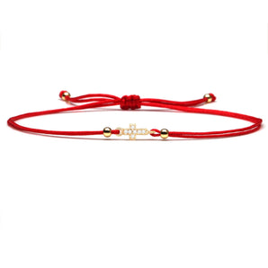 Red string bracelet with a gold charm, adjustable fit, placed neatly with a focus on its vibrant carmine color and circular gold charm, highlighting its appeal as a lucky and spiritual fashion accessory.